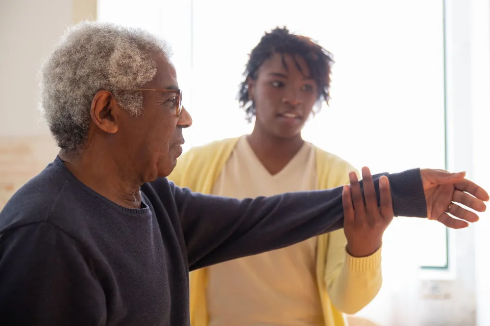 Caregiver assisting an elderly man with exercise, representing recovery care